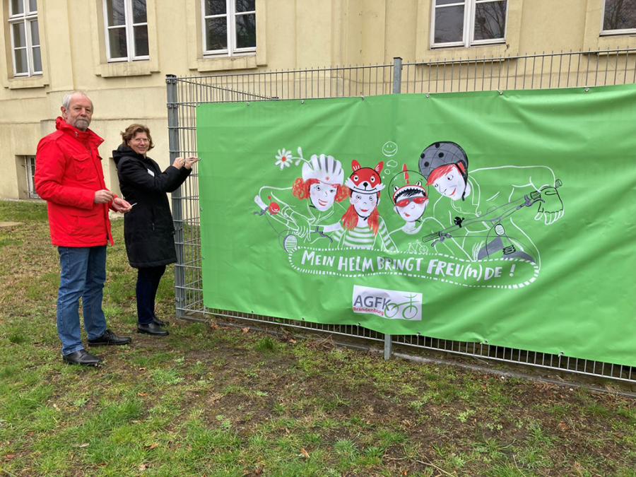 Zu sehen ist die Anbringung des Aktionsmotivs „Mein Helm bringt Freu(n)de“ am Landratsamt in Lübben.