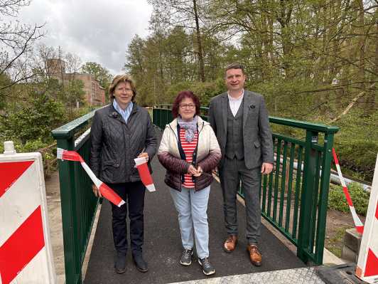 Drei Personen stehen auf einer Fußgängerbrücke und durchschneiden ein Flatterband