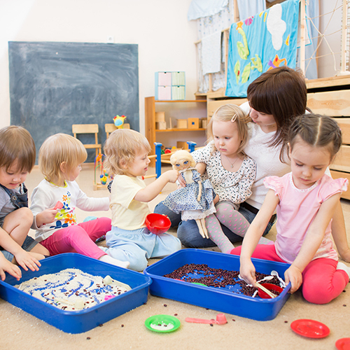 Eine Gruppe von Kleinkindern spielt mit der Erzieherin. 