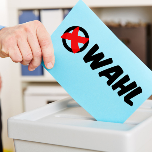 Sie sehen ein Symbolbild zur Wahl mit Stimmzettel und Wahlurne.