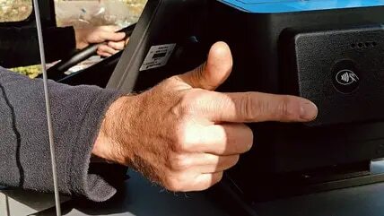Kontaktloses bezahlen RVS Eine Hand zeigt auf ein Kartenlesegerät in einem Bus.