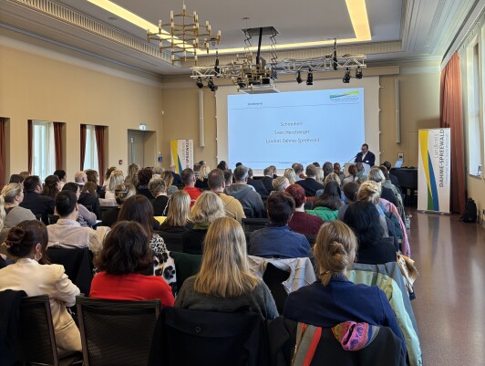 Landrat Herzberger steht vor einem sitzenden Publikum