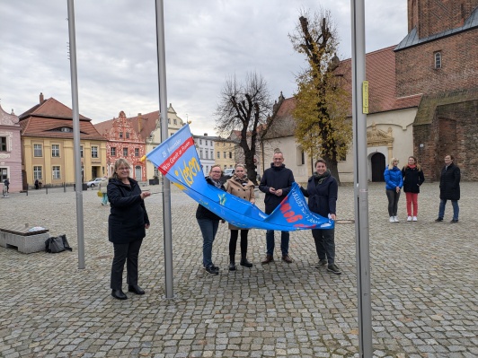 Bürgermeister der Stadt Luckau Gerald Lehmann sowie Mitarbeitende der LDS-Gleichstellungsbeauftragten hissen die Fahne zum internationalen Tag gegen Gewalt an Frauen am Rathaus in Luckau.