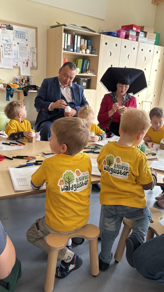 Erwachsener Mann sitzt mit Kitakindern am Tisch und bemalt Ostereier