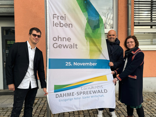 Bürgermeister der Stadt Lübben, Jens Richter sowie Gleichstellungsbeauftragte Dr. Corinna Junker hissen die Fahne zum internationalen Tag gegen Gewalt an Frauen am Lübbener Rathaus.