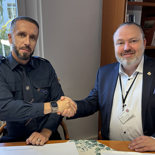 Zwei Männer schauen in die Kamera. Ein Mann trägt eine Polizeiuniform.